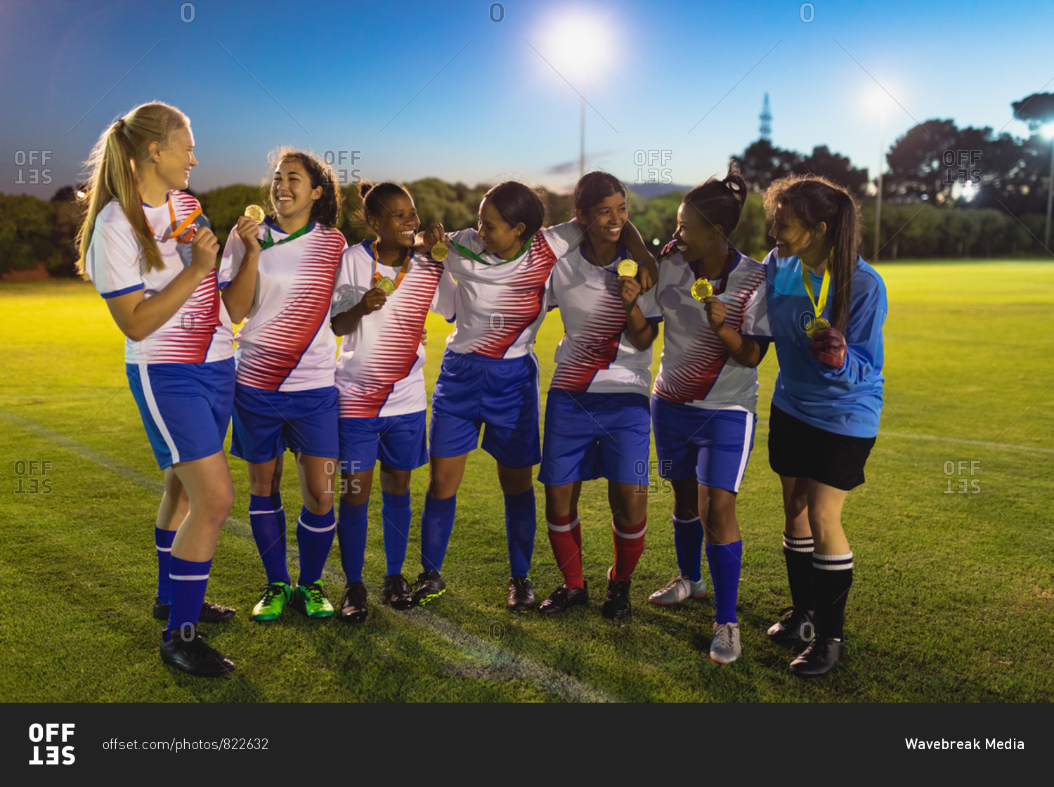 Front view of diverse female soccer team showing medal to each other at sports field