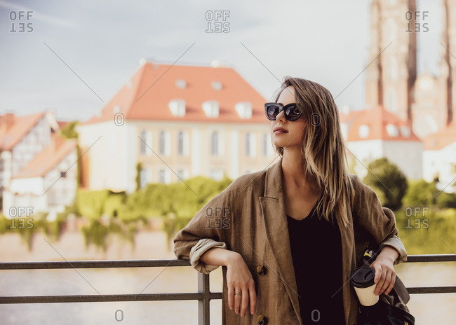 Young style woman in sunglasses stay near railing with old city on background