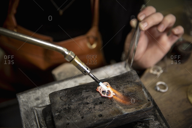 Close-up of goldsmith heating metal with welding torch to make jewelry in workshop