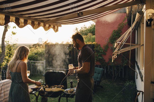 Male and female friends grilling food while having wine in party