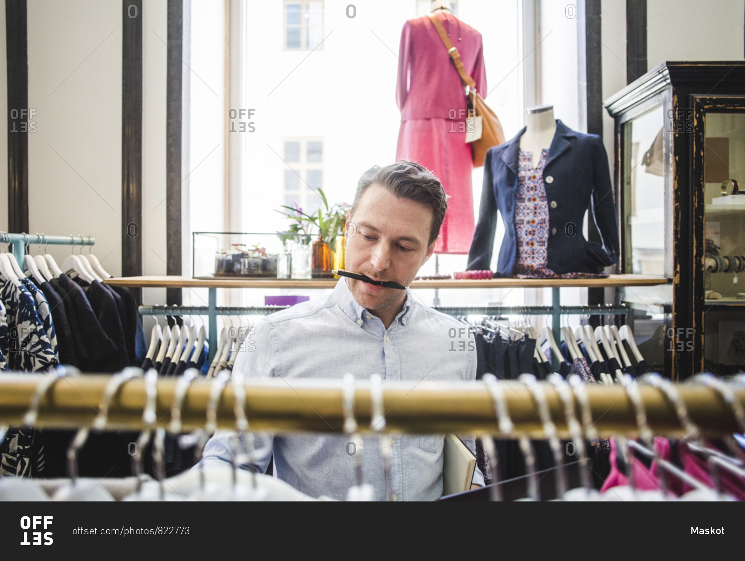 Salesman carrying pen in mouth while looking at clothes rack