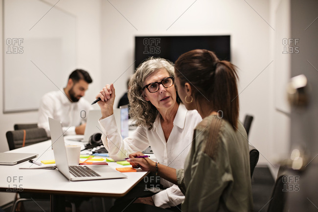 Businesswomen discussing over laptop while male colleague working in background