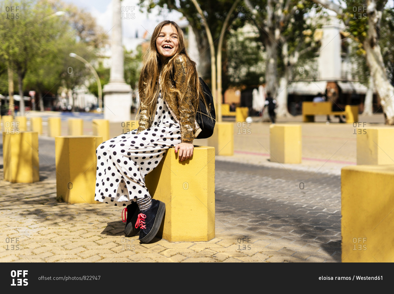 Portrait of stylish girl sitting on bollard laughing