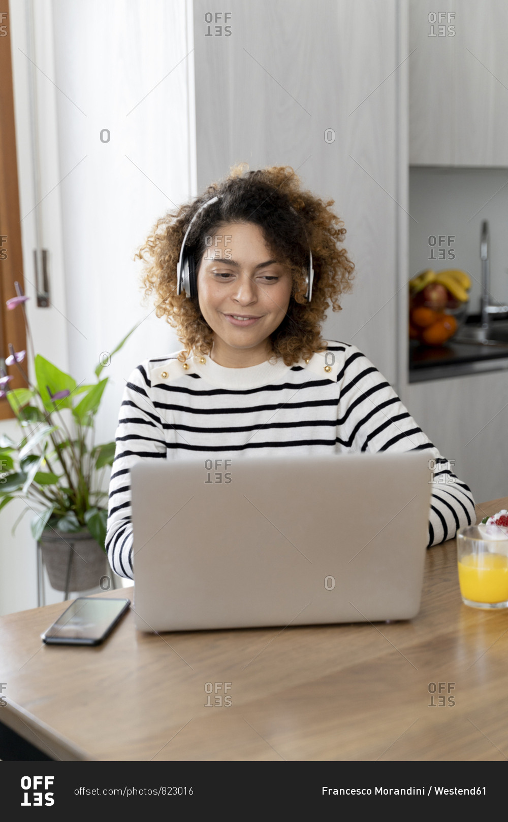 Woman sitting at table- using laptop with headphones