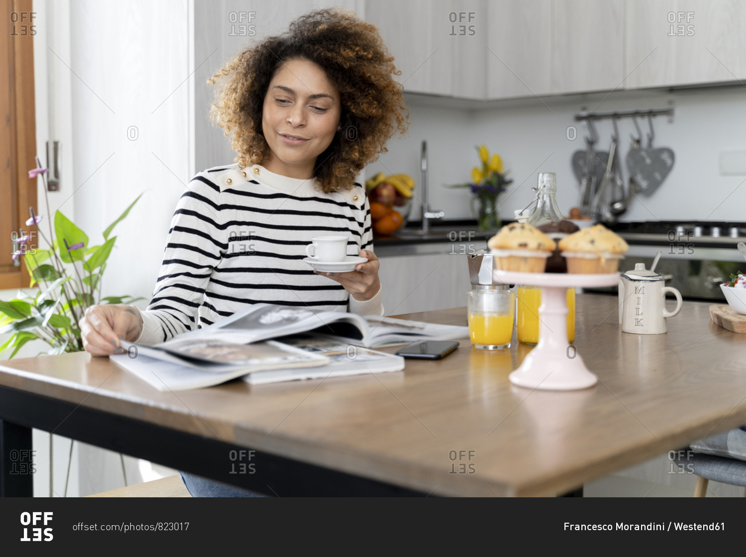 Woman sitting in kitchen- reading magazines and drinking coffee