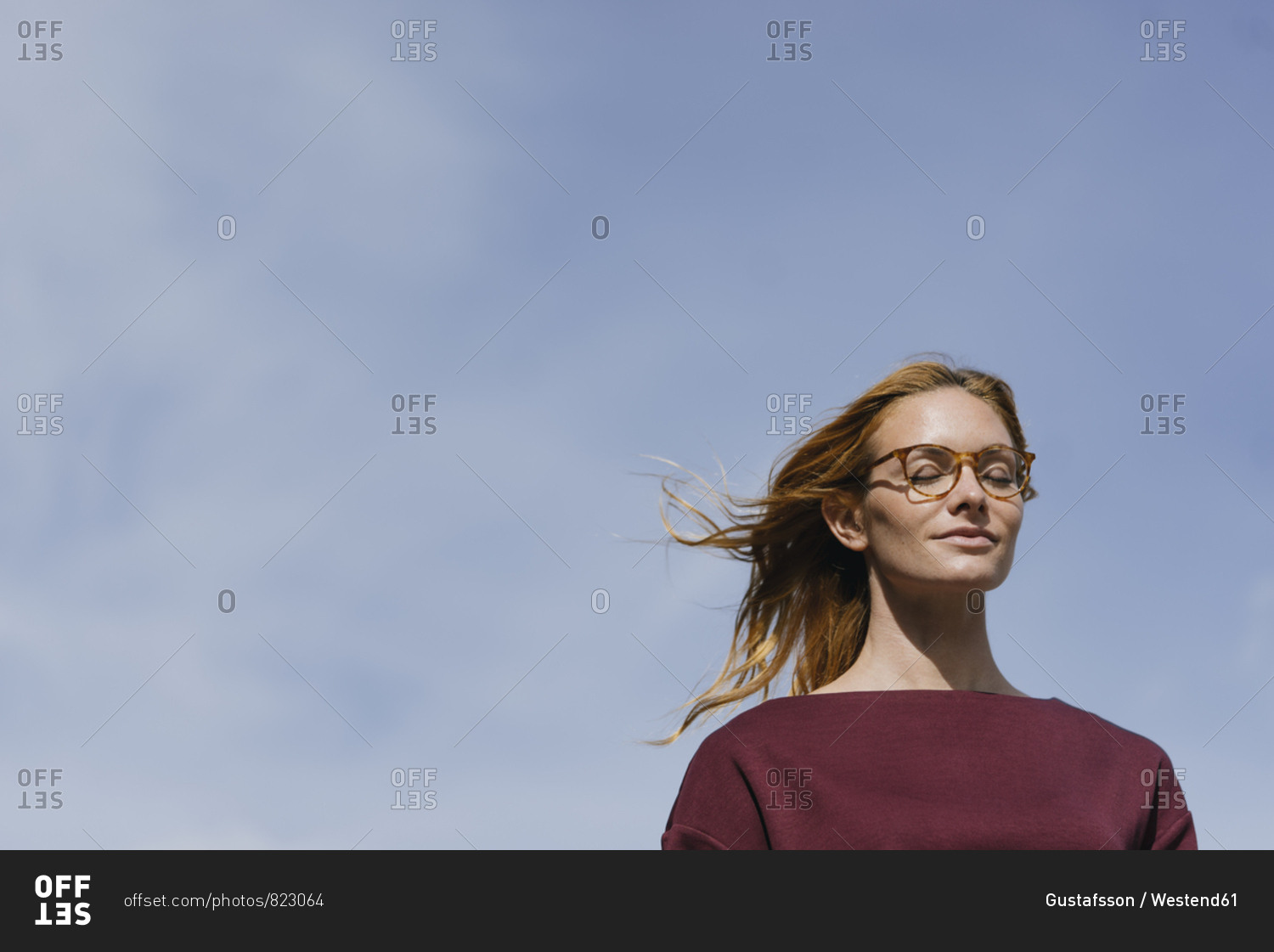 Portrait of young woman with glasses and closed eyes under blue sky