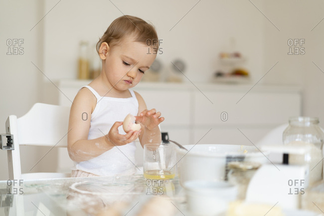 Girl making a cake in kitchen at home cracking an egg