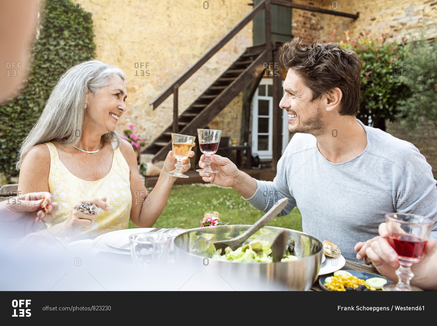 Happy family eating together in the garden- clinking glasses
