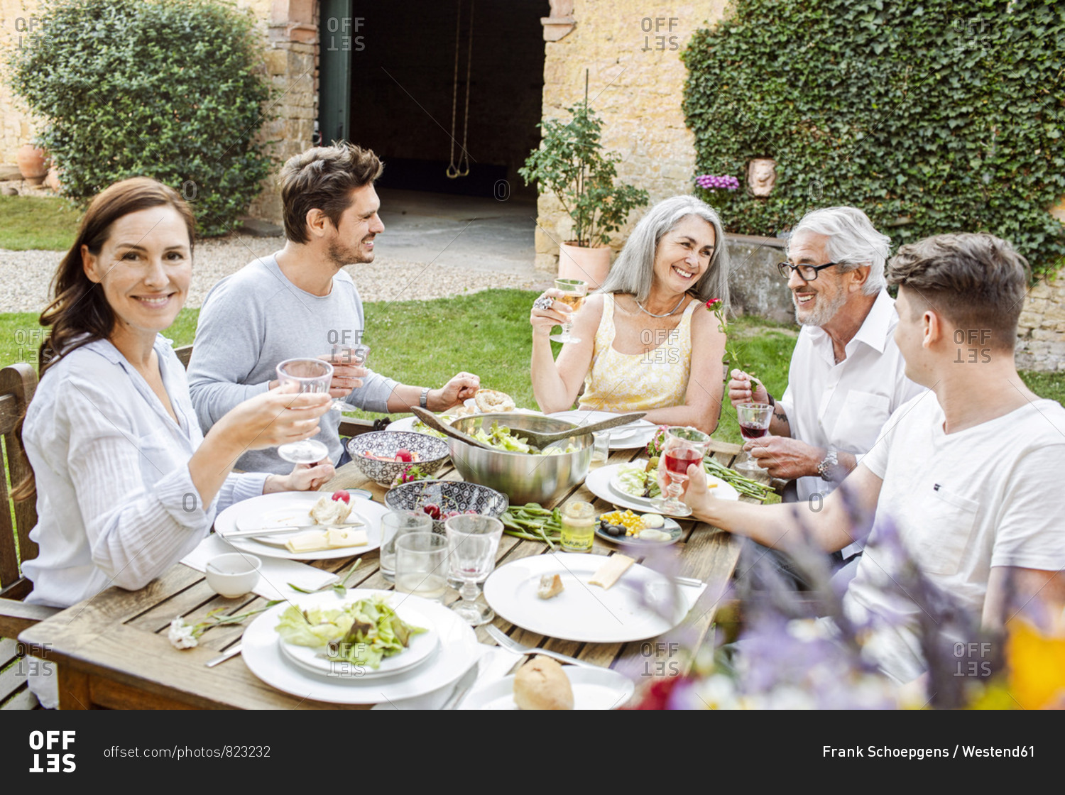 Happy family eating together in the garden- clinking glasses