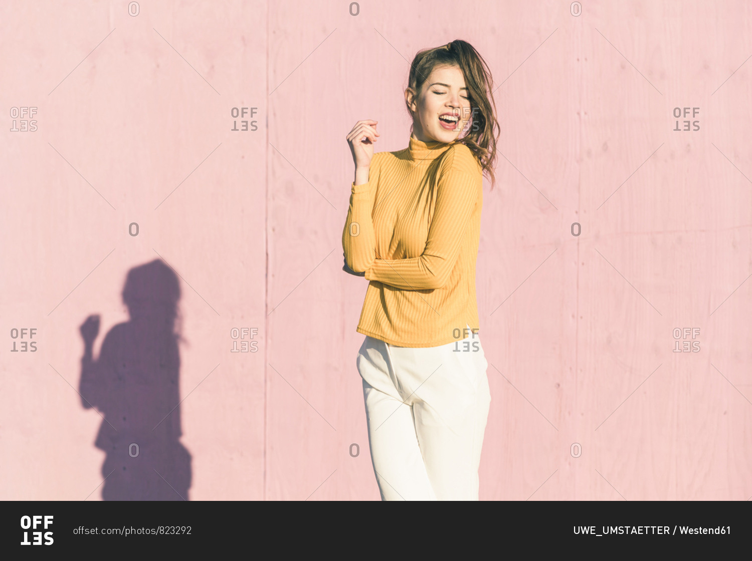 Happy young woman in front of a pink wall