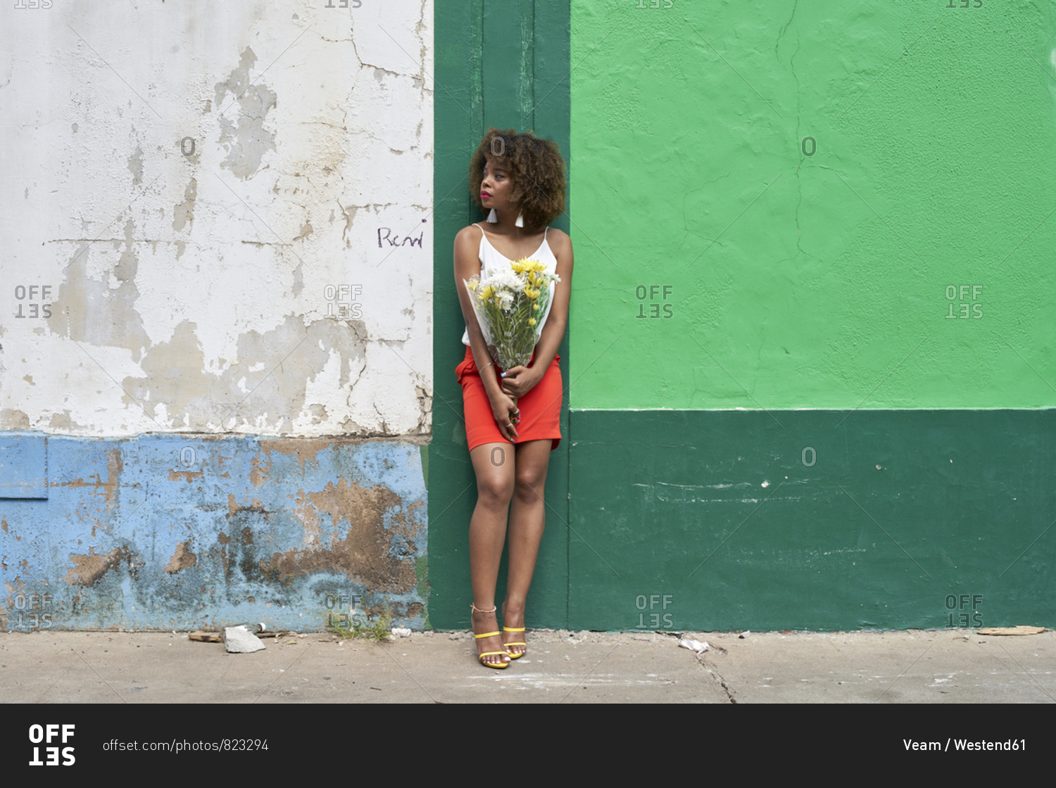 Young woman with bunch of flowers leaning against wall looking around