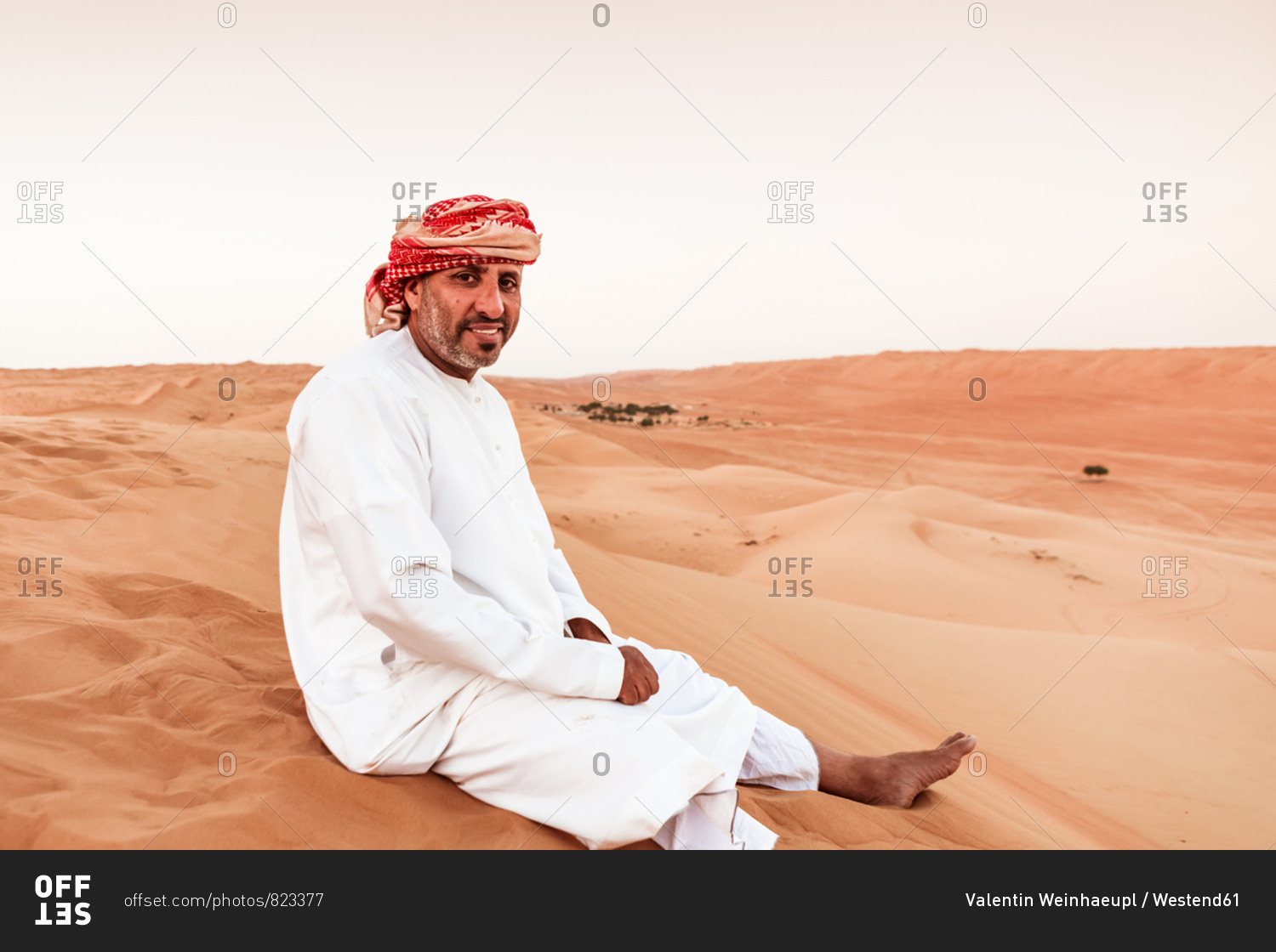 Bedouin in National dress sitting on sand dune in the desert- Wahiba Sands- Oman
