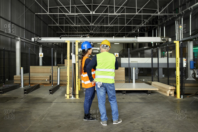 Rear view of male and female worker standing in factory workshop