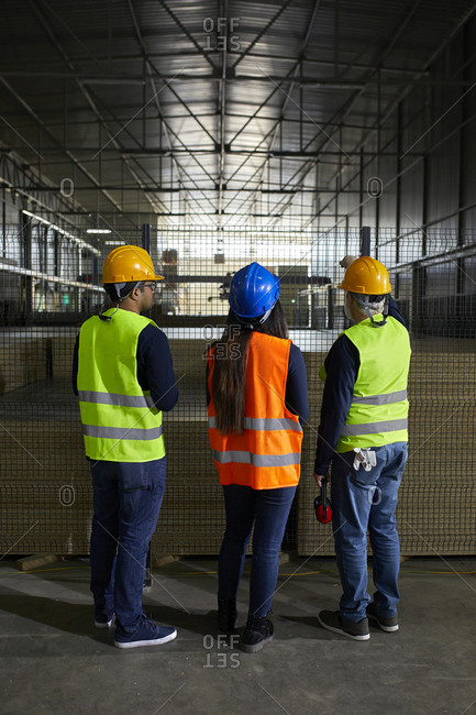 Rear view of workers standing at grid in factory