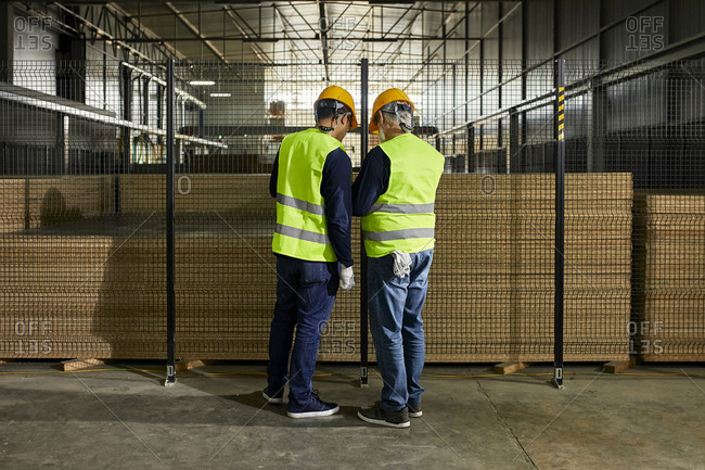 Rear view of workers standing at grid in factory