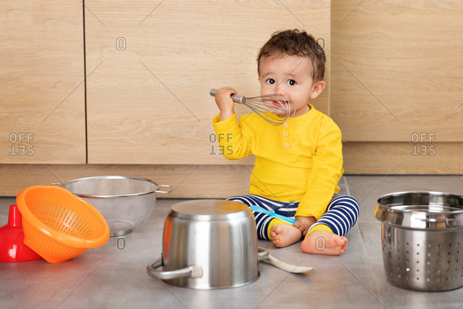 Cute baby playing with utensils in kitchen