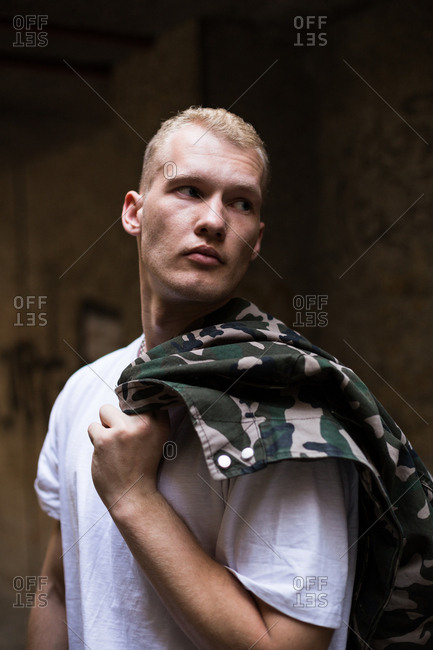 Handsome guy holding military jacket on shoulder and looking away
