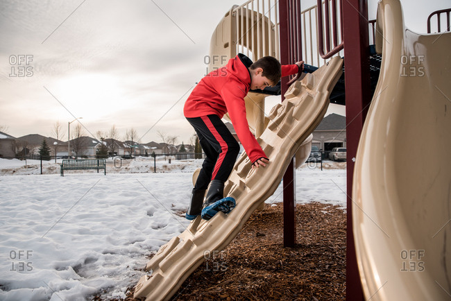 Boy climbing on playground structure in a snowy park on winter day.