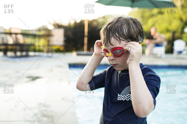 Young Boy Wearing Red Goggles Stands in Pool in Summertime