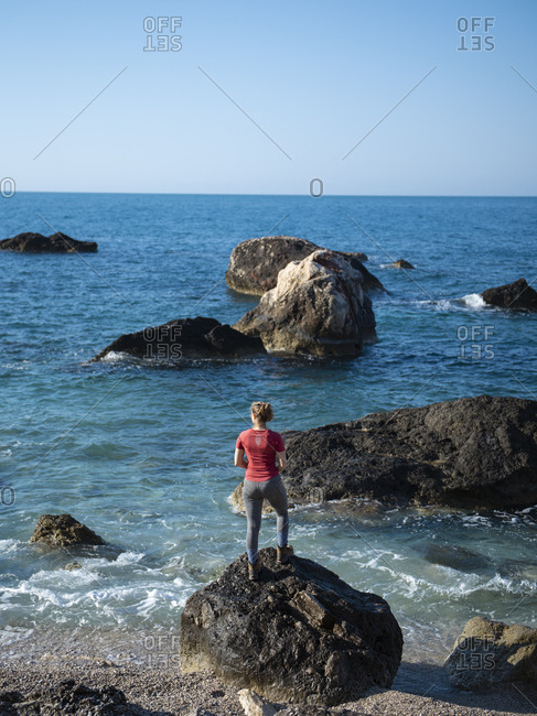 Rear view of young woman standing on the rock and looking at the sea