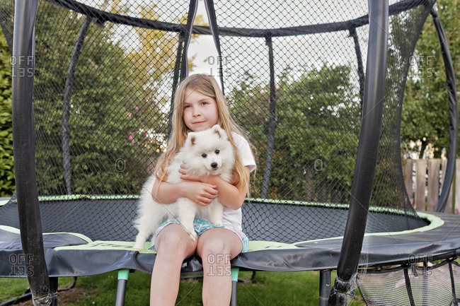 Young girl sitting on a trampoline holding a small fluffy white dog