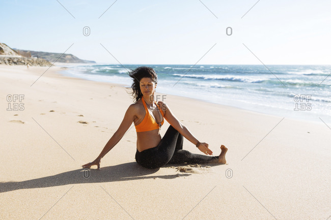 Mature woman practicing yoga on beach, on a very windy and sunny day.