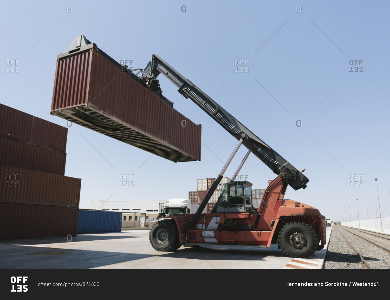 Crane lifting cargo container near railway tracks on industrial site