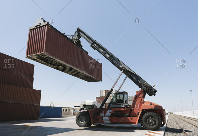 Crane lifting cargo container near railway tracks on industrial site