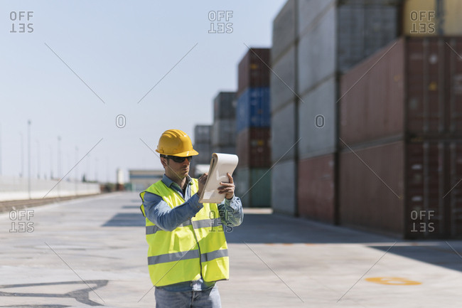 Worker with a notepad near cargo containers on industrial site
