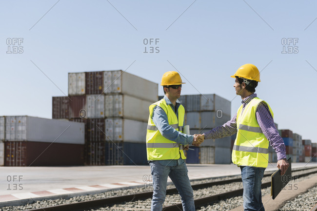 Workers shaking hands on railway tracks near cargo containers on industrial site