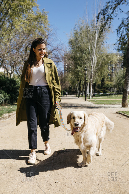 Happy woman going walkies in city park with her Labrador Retriever