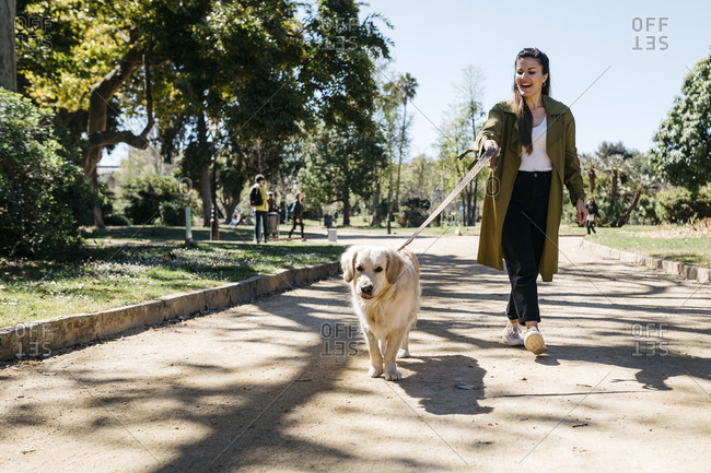 Happy woman going walkies in city park with her Labrador Retriever