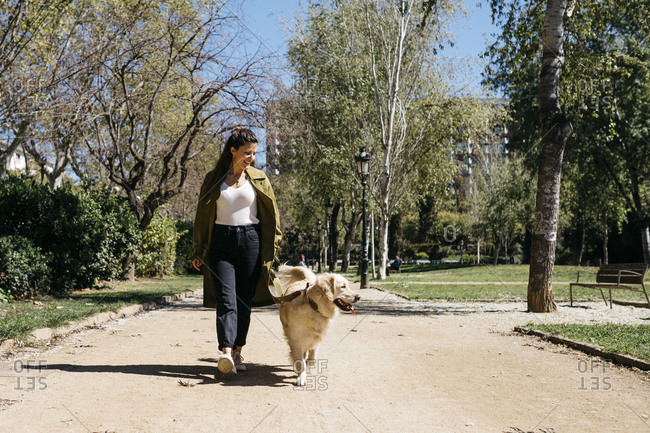 Happy woman going walkies in city park with her Labrador Retriever