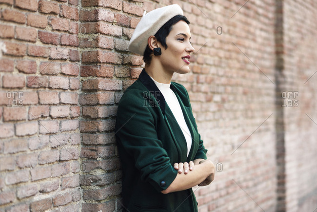 Fashionable young woman wearing a beret and a green jacket at a brick wall