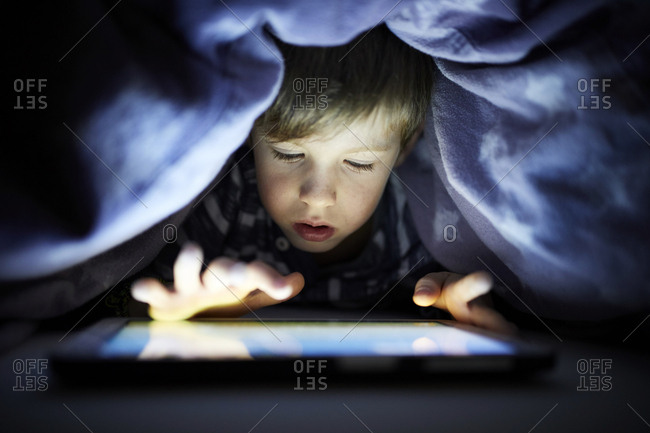 Little boy playing secretly with his digital tablet- hidden under blanket