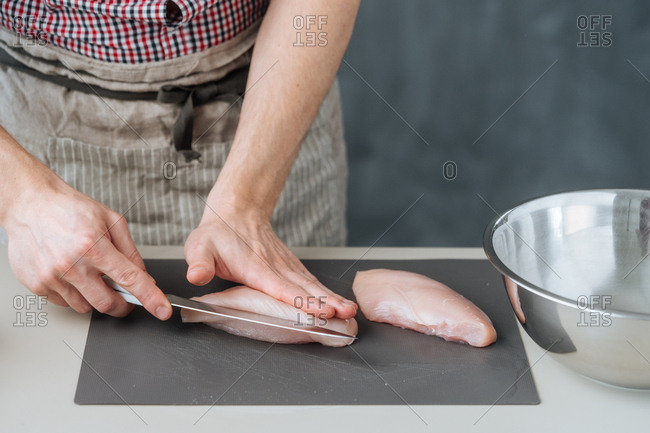 Man in apron slicing chicken breasts with knife