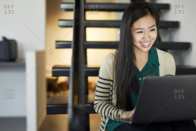 Smiling businesswoman using laptop computer while sitting on steps in office
