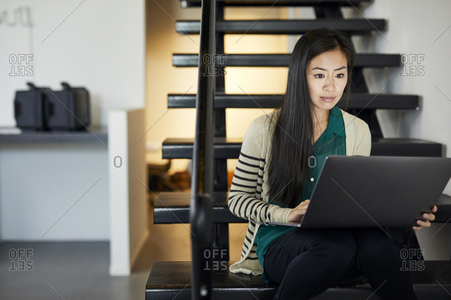 Confident businesswoman using laptop computer while sitting on steps in office