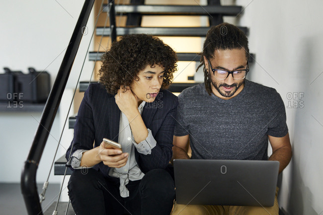Colleagues doing research over laptop computer while sitting on steps in office