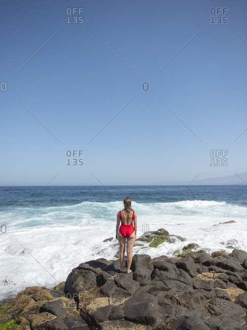 Rear view of woman standing on rocky coast and looking at ocean waves