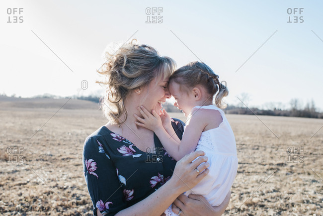 mother and daughter cuddling and laughing whilst standing in a field