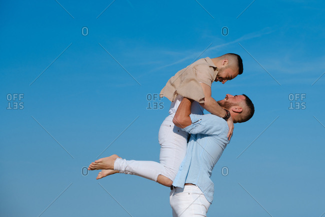Side view of happy gay man lifting up and going to kiss boyfriend on deserted beach on summertime