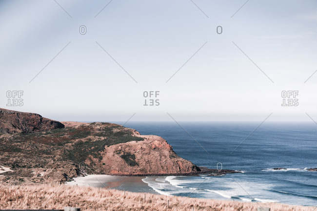 Foam of blue waves and rocky mossy shore on background of calm sky in daylight