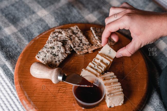 Crop view of woman hand taking delicious snack of cheese with crackers and marmalade on wooden board on bed