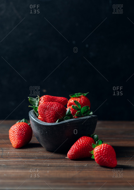 Fresh ripe strawberries in black concrete bowl on wood background