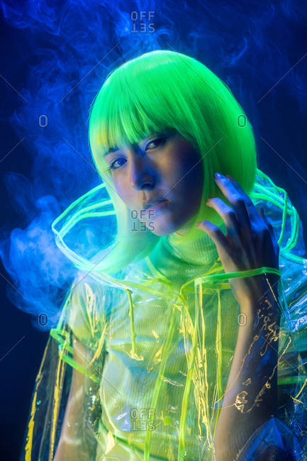 Young pretty unusual Asian woman in plastic transparent raincoat and yellow hair smoking in fluorescent light