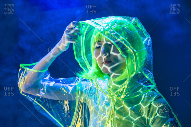 Young pretty unusual Asian woman in plastic transparent raincoat and yellow hair smoking in fluorescent light