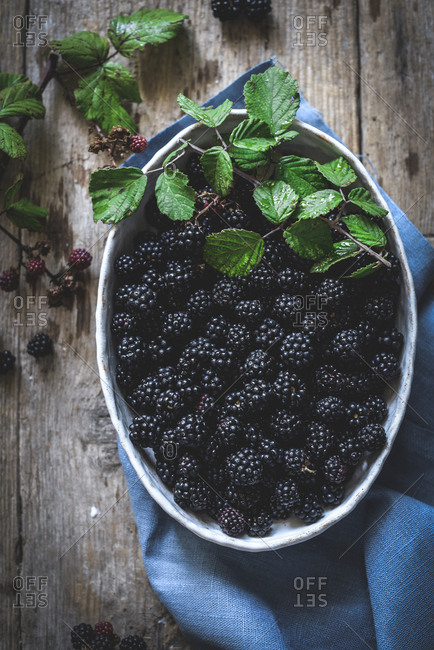 From above tasty fresh blackberries serving in bowl on wooden background with blue napkin