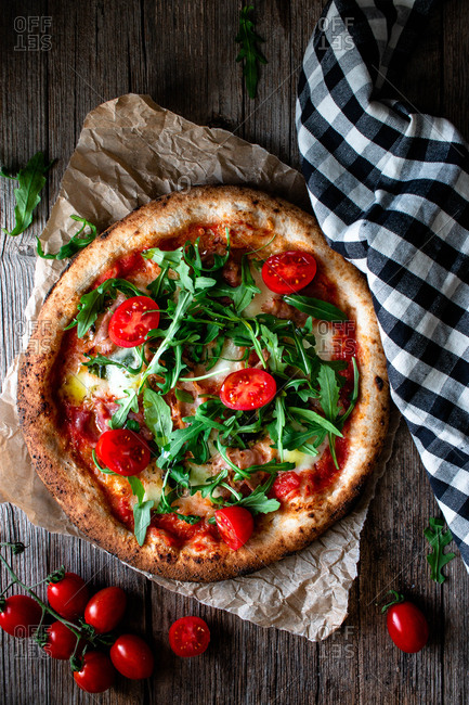 From above delicious pizza with tomato and salad placed with checkered towel on wooden background