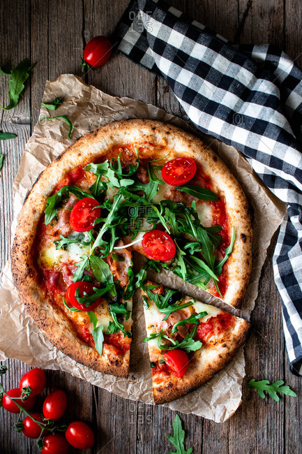 From above delicious pizza with tomato and salad placed with checkered towel on wooden background